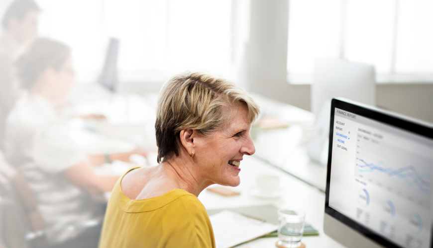 A woman smiles at her desk, working on a computer, illustrating the theme of choosing between CRM vs ERP software.